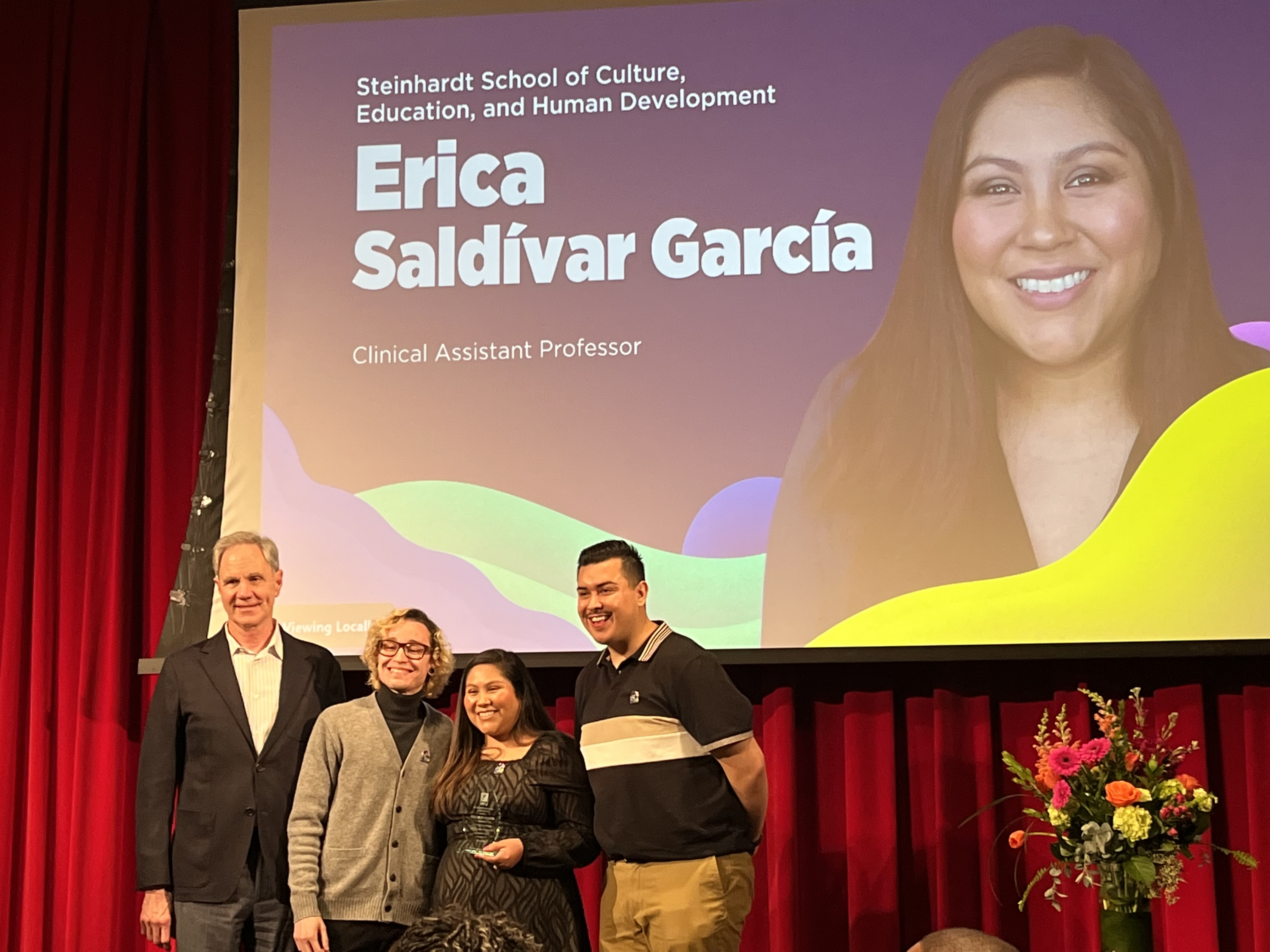 Erica with colleagues on a stage in front of a slide introducing her
